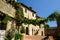 Alley of the city of Assisi with stone facades of historic houses. Arbor with climbing vine plant and flags on the walls of