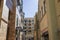 An alleyway with a red brick footpath surrounded by brown apartments and shops and a woman walking with a clear blue sky