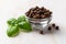 Allspice jamaica pepper in a in a glass bowl and fresh basil leaves on a white wooden table. Close-up of Dried pimento berries for