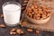 Almond milk in a glass and almonds in a bowl on dark wooden background