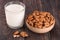 Almond milk in a glass and almonds in a bowl on dark wooden background