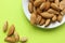 Almonds are not cleaned. Some nuts lie on a white plate on the right side, not fully visible. Five almond nuts lie separately on a