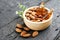 Almonds oil in wooden bowl with roasted almonds on black wooden plank