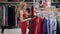 Alone buyer girl is strolling in sales area in trendy fashion store with female clothes, looking on hangers with