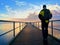 Alone man on pier and look over handrail into water. Sunny sky, smooth water level