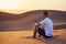 Alone man sitting on sand dune and using phone