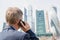 Alone middle-aged gray-haired businessman in a blue suit calling by phone standing opposite Moscow City skyscrapers.Low angle view