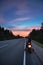 Alone motortraveler with own motorbike resting on roadside at dusk time with sunset on country route