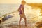 Alone preschooler boy walking barefoot along the seashore during summer holidays. Child having fun in waves on sunset. Family