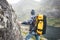 Alone professional traveler with backpack on high mountain standing on the edge cliff rock and looking away