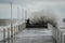 Alone surfer in wetsuits with surfboard on a city pier amid powerful waves in Australia. Concept: confrontation between the