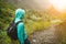 Alone traveler with backpack walking down cobbled trekking trail towards green valley. Sun flares on hoziron. Santo