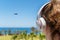 Alone woman on a beach in headphones listen music looking on the sea, palm trees, plane. Female relaxation at summer vacation.