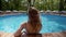 Alone woman is relaxing in pool, back view, tilt up panoramic from sky with tops of pine