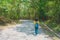 Alone woman traveller or backpacker walking along contryside road among green trees.