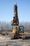 The alone yellow excavator on the roadside of asphalt road on the background of blue sky and forest