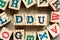 Alphabet block in word DDU abbreviation of Delivered Duty Unpaid with another on wood background
