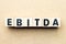 Alphabet block in word EBITDA abbreviation of earnings before interest, taxes, depreciation and amortization on wood