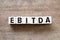 Alphabet block in word EBITDA abbreviation of earnings before interest, taxes, depreciation and amortization on wood background