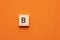 Alphabet letter B on wooden square tile - Orange foamy background