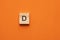 Alphabet letter D on wooden square tile - Orange foamy background