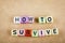 Alphabet letter dice text on desk, spelling HOW TO SURVIVE