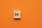 Alphabet letter H on wooden square tile - Orange foamy background