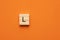 Alphabet letter L on wooden square tile - Orange foamy background