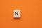 Alphabet letter N on wooden square tile - Orange foamy background