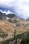 Alpine gorge with yellow autumn grass and pine trees on slopes, winding trekking path and wires from high voltage power line