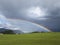 Alpine landscape with beautiful rainbow. Mountains, meadows and pastures with sunbow.