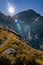 Alpine landscape in the Lord of the Rings style. In the foreground is a grassy expanse with a path running across it