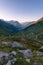 Alpine landscape photographed at first light, with a winding road running through the mountains following a stream.