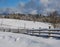 Alpine mountain snowy winter fir forest and snow drifts near wood fence on secondary countryside road wayside