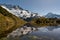 The alpine tarn at the summit of the Sealy Tarns track with mirror reflections of the snow covered mountains in the Aoraki