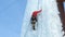 Alpinist man with ice tools axe climbing a large wall of ice.