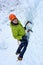 Alpinist man with ice tools axe in orange helmet climbing a large wall of ice. Outdoor Sports Portrait