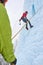 Alpinist woman with ice tools axe in orange helmet climbing a l