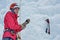 Alpinist woman with ice tools axe in orange helmet climbing a l