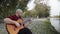 An alternative man sitting beside lake and playing guitar