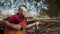 Alternative man sitting at park and singing while playing guitar