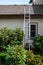 Aluminum extension ladder leaning against a brown residential house with wood siding, roof access for fall maintenance