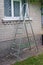 An aluminum folding garden staircase stands near a brick wall of a rural house