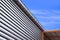 Aluminum louver wall with steel rain gutter and arcade roof outside of warehouse building against blue sky