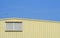 Aluminum louver on yellow corrugated steel warehouse wall against blue sky background