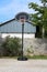 Amateur metal and plastic basketball hoop mounted on stone tiles backyard in front of stone wall surrounded with trees and cloudy