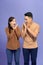 Amazed asian couple expressing shock, purple studio background