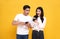 Amazed attractive young Asian couple looking message at smartphone together isolated on yellow background