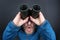 Amazed bearded man looking up in binoculars on grey background