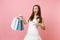 Amazed bride woman in white wedding dress pointing index finger on multi colored packages bags with purchases after